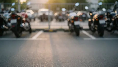 Soft focus background of a motorcycle parking lot with warm sunset light, asphalt, white lines, and motorcycle silhouettes, ideal for text overlay.