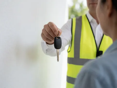 Valet in reflective vest handing a car key to a client in a professional parking setting under natural light
