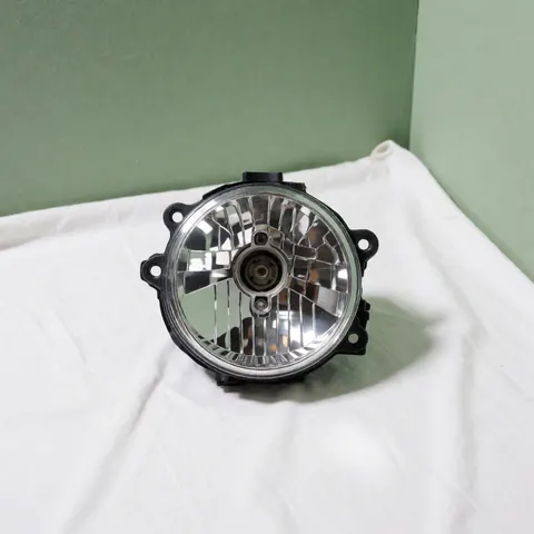 New and clean car headlight placed on white fabric with a pale green wall background, suitable for vehicle recycling services.