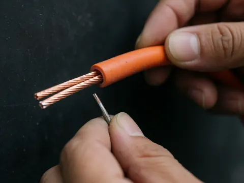Close-up of an orange THW-2 insulated copper conductor being handled by a hand against a dark professional background.