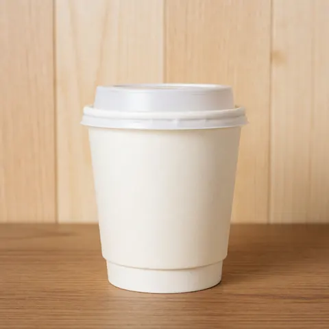 A disposable coffee cup with a white lid placed on a wooden table against a light wood panel background with bright clean lighting