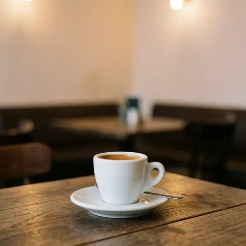 White cup of espresso on a plate with spoon on rustic wooden table in warm cafe interior