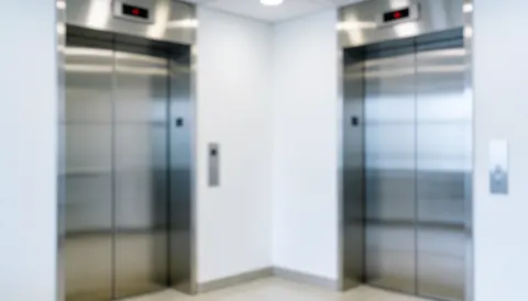 Professional office hallway background featuring two stainless steel elevator doors, white walls, and even lighting, ideal for commercial text overlays.