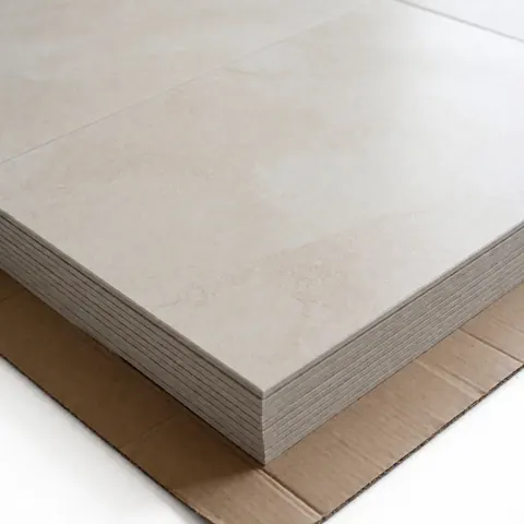 A neat stack of beige porcelain tiles with a stone texture resting on protective cardboard, lit for commercial product catalog use.