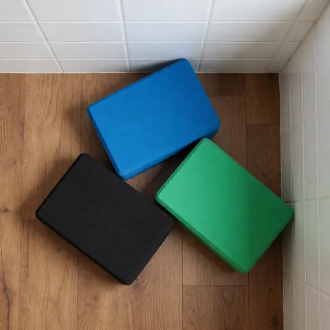 Three yoga blocks in blue, green, and black arranged on a wooden floor near white tiled walls, ideal for fitness and stability.