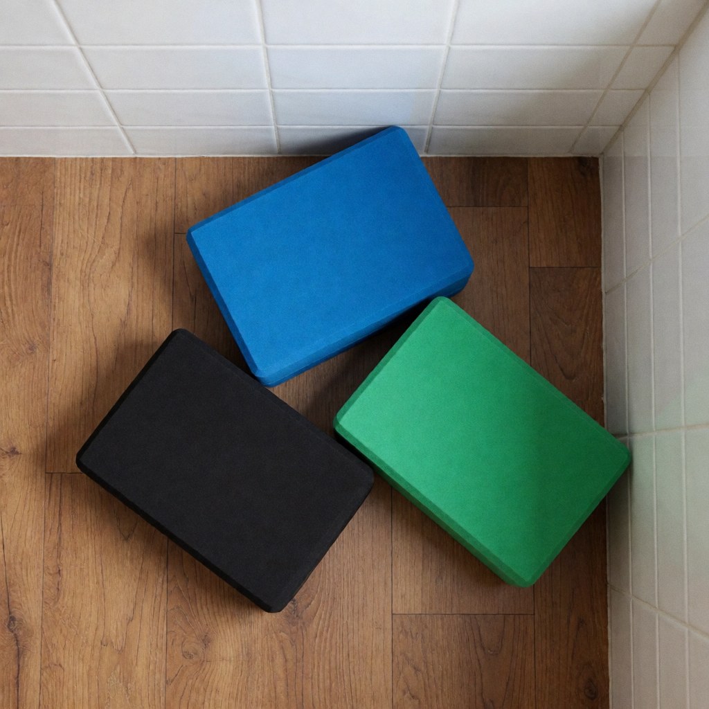 Three yoga blocks in blue, green, and black arranged on a wooden floor near white tiled walls, ideal for fitness and stability.