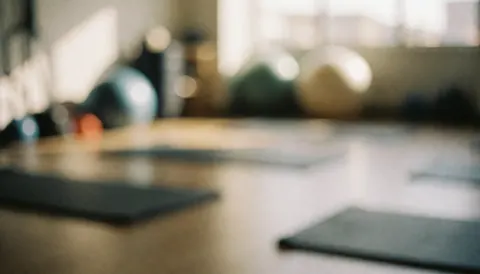 Soft focus background of a rehabilitation room with exercise mats and therapy balls, featuring warm professional lighting suitable for personal training text overlays.