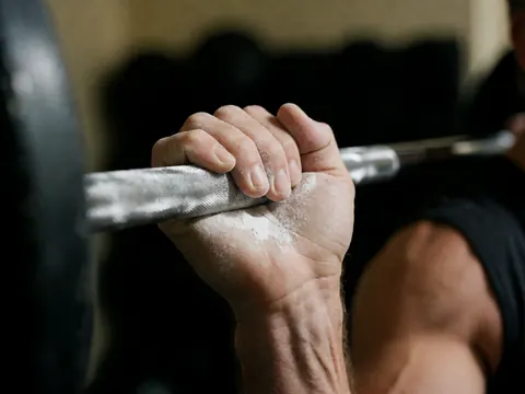 Close-up of a hand with white magnesium powder gripping a barbell against a dark blurred background, showing realistic texture and detail.