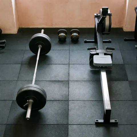 Overhead view of a barbell, two kettlebells, and a rowing machine on a black floor against terracotta walls, ideal for fitness training