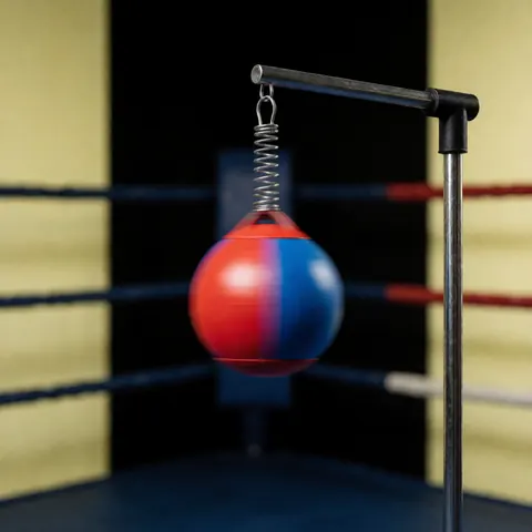 Red and blue speed ball hanging from a spring in a boxing ring corner with dark background and yellow walls for reflex training
