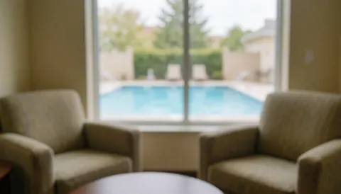 Upholstered armchairs in a lounge area overlooking a swimming pool, creating a relaxed and warm atmosphere suitable for text overlays.