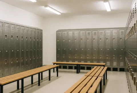 Clean and organized locker room featuring metal lockers and wooden benches under fluorescent lighting, suitable for martial arts students.