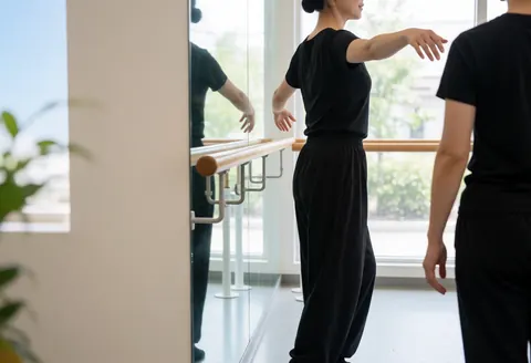 A dancer practicing in a studio with a barre and mirror, natural light, space for text