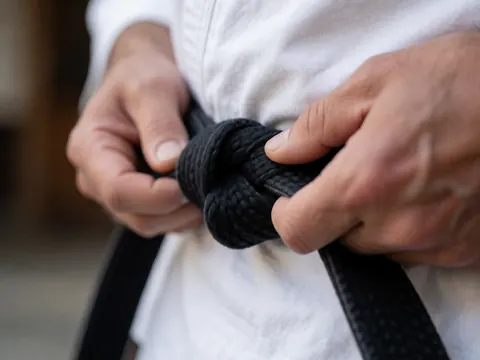 Close-up of hands tying a black belt on a white martial arts uniform, showing fabric texture and blurred background