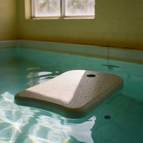 Non-slip swimming kickboard floating in clear water with sunlight reflections and yellow walls in the background