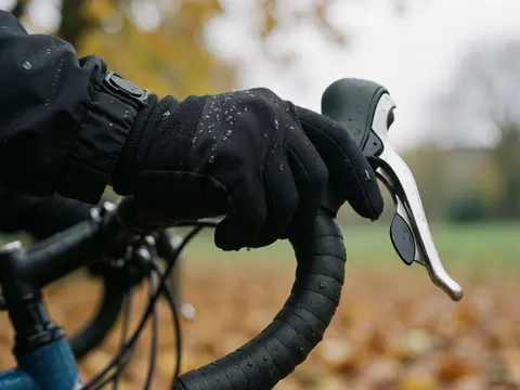 Close-up of a black glove holding a wet bike handlebar with raindrops and blurred leaves in the background