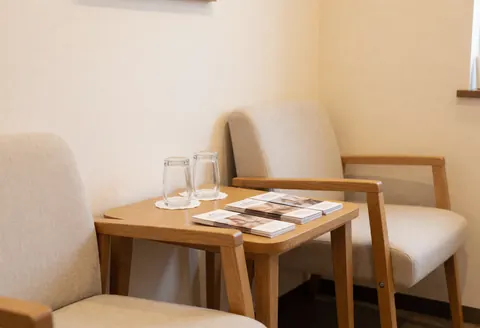 Reception area featuring comfortable chairs and a wooden table holding water and brochures against beige walls.