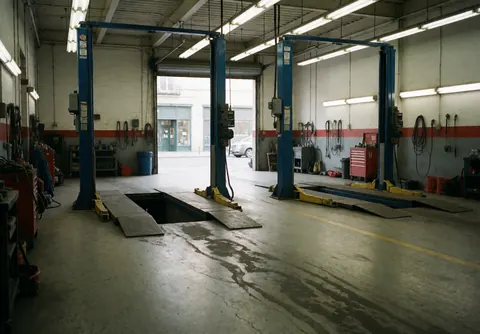 Hydraulic lifts in a tire repair shop with oil stains on the concrete floor, fluorescent lights, and tools hanging on the walls.