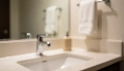 Warmly lit bathroom background featuring a faucet, mirror, and white towel, suitable for commercial text overlays