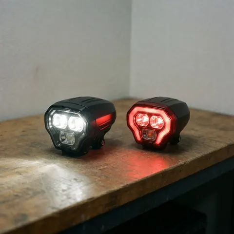 Two lit bicycle LED lights, one white and one red, placed on a textured wooden bench, highlighting component details with bright illumination.