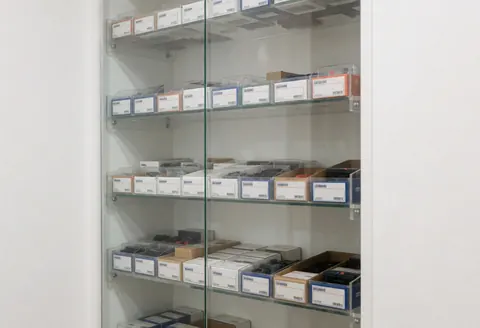 Glass display case with shelves full of electronic component boxes, white walls, even lighting, ideal for repair shop