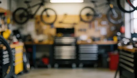 Out of focus bike repair shop interior featuring hanging bicycles, toolboxes, and workbenches, providing a clean backdrop for text or logos