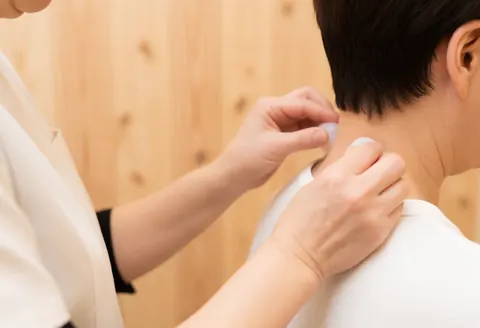 Close-up of hands using glass cups on a client's neck during a cupping massage session with a natural wood background