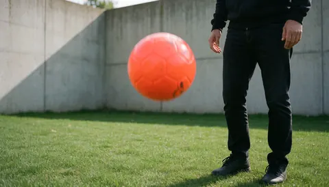 Orange soccer ball rolling on green grass with concrete wall background for outdoor training scene
