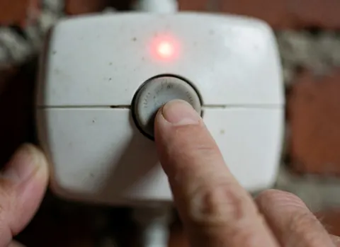 Close-up of a finger pressing a control button with a red light against a brick wall background