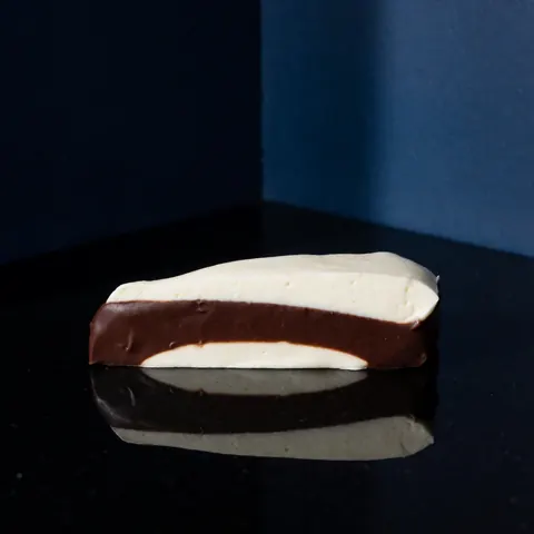 Chocolate cake with cream on a reflective black surface, dramatic lighting, dark blue background, soft textures and visible layers
