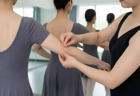 Dance instructor correcting a student's arm position during a practice session in a studio with mirrors and natural light