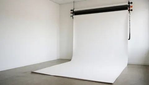 Empty photography studio featuring a seamless white backdrop, polished concrete floor, and soft natural lighting ready for professional portrait sessions