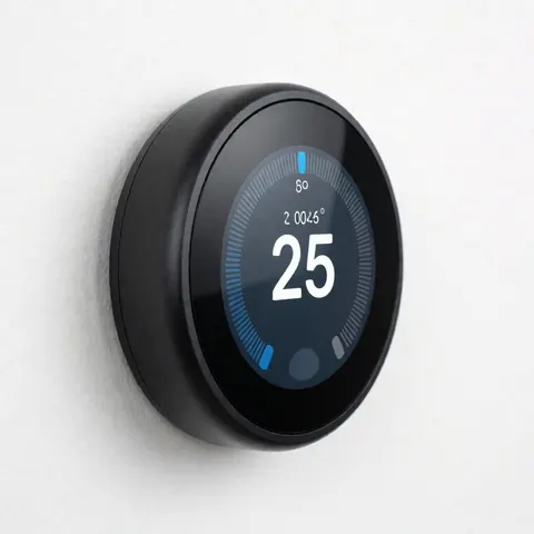 Close-up of a black digital thermostat with a blue display screen showing temperature, mounted on a plain white wall for HVAC and boiler repair services