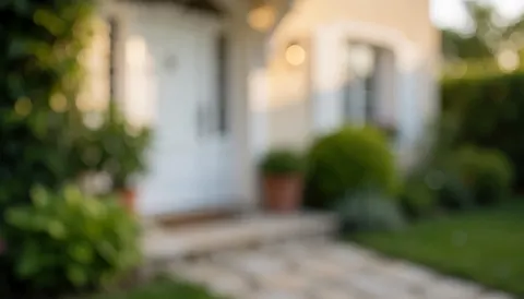 Soft background of a villa entrance with a white door, green foliage, and stone path illuminated by warm sunset light, ideal for text overlay.
