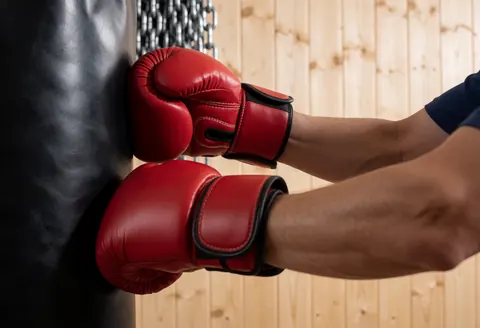 Close-up of red boxing gloves hitting a black punching bag with chains and wooden wall in background