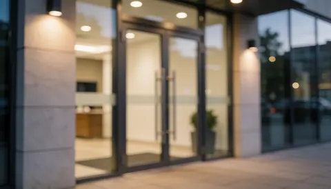 Blurred business entrance background featuring glass doors, metal frames, and warm light, suitable for text overlay