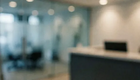 Blurred background of a glass storefront reception with glass partitions, desk, and warm lighting, ideal for text overlay.