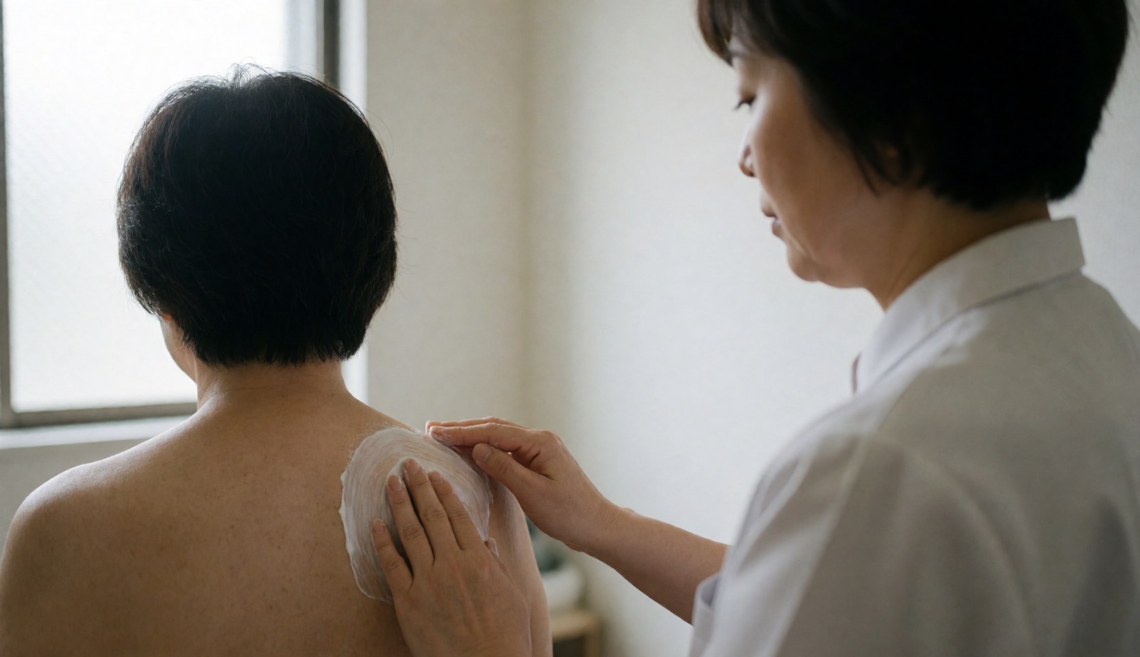 Therapist applying cream to a client's shoulder in a clinic with natural light, demonstrating cupping massage technique.