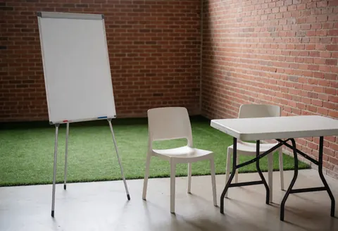 Whiteboard on table with chairs in outdoor soccer tactical area on artificial grass near brick wall