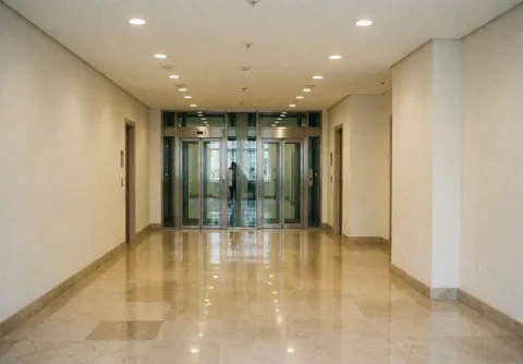 Spacious lobby featuring polished marble flooring, glass elevator doors, and warm white walls creating a clean professional atmosphere.