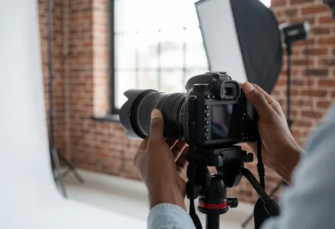 Close-up of hands adjusting the focus ring on a dslr camera mounted on a tripod in a studio with a brick wall and softbox