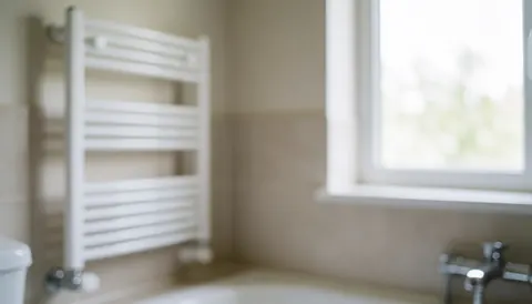 Clean bathroom background featuring a white towel rack, neutral walls, and natural light from a window, suitable for professional cleaning services.