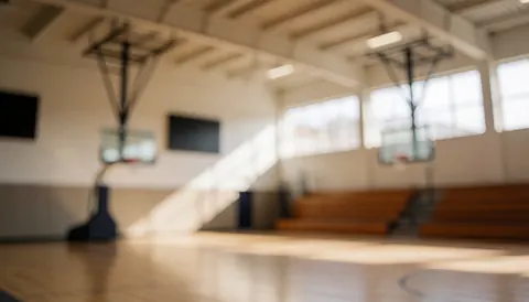 Out of focus basketball court interior featuring hoops, benches, and natural light, suitable for text overlay