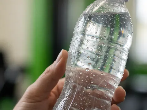 Close-up of a plastic water bottle with condensation droplets in a gym setting, highlighting hydration and fitness details.