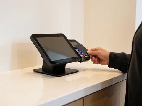 A hand uses a card on a payment terminal on a clean counter with warm white walls and bright lighting.