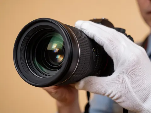 Close-up of a white-gloved hand adjusting the focus ring on a professional camera lens against a beige background