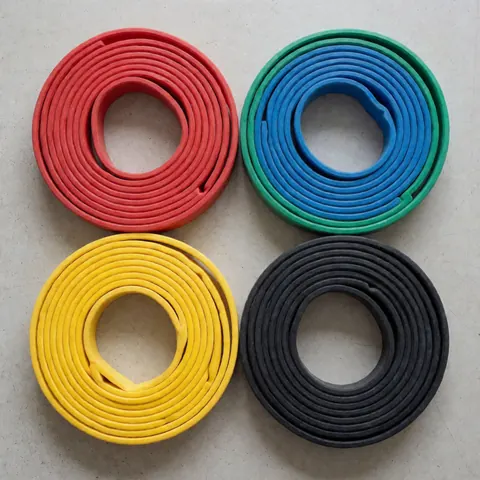 Four colorful resistance bands in red, blue, yellow, and black rolled up on a light concrete floor for physical training products.
