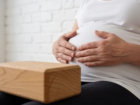Hands placed gently on the abdomen during a yoga session with a wooden block and white brick wall in the foreground