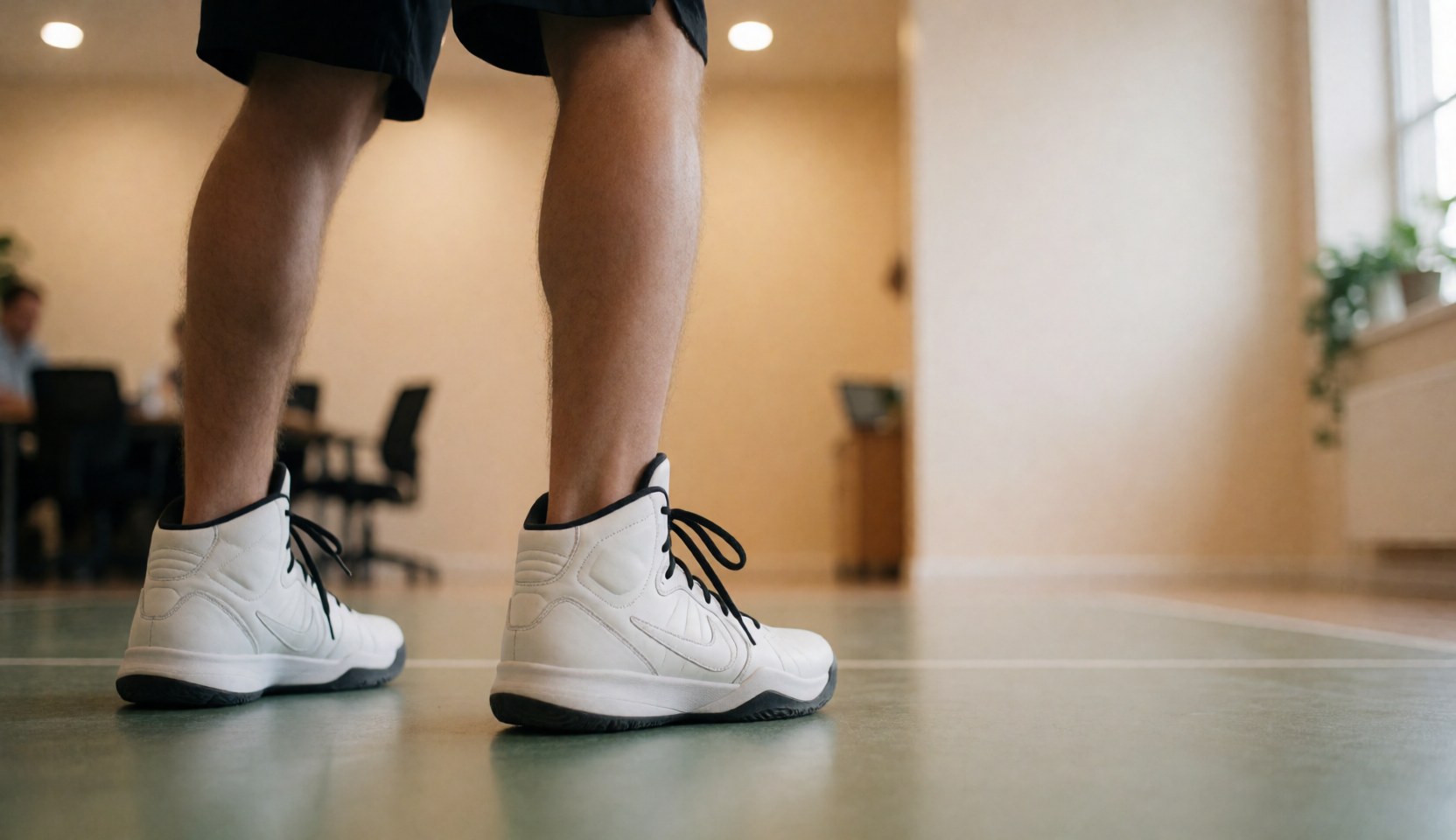 White basketball shoes with black laces on a gym floor, viewed from behind, ideal for a basketball coach website hero section