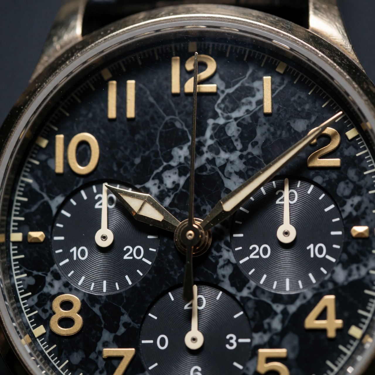 Close-up of a wristwatch with a black marble dial, gold numerals, and chronograph subdial details for product photography.
